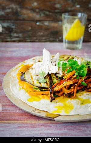 Tirato avvolgere il pollo, la carota, melanzane grigliate, curry hummus e erbe sul tagliere Foto Stock