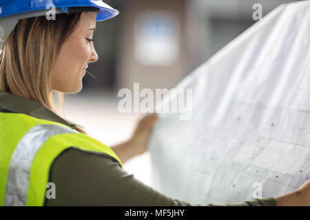 Donna che indossa elmetto guardando al piano di costruzione Foto Stock