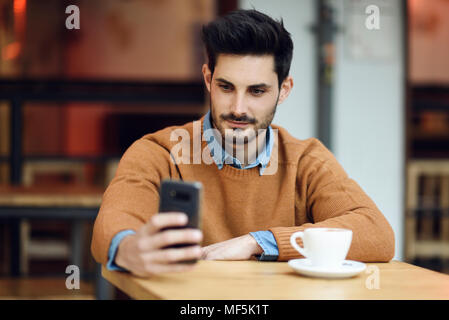 Spagna, Andalusia, Granada. Attraente giovane con moderni acconciatura seduto in un bar caffetteria guardando il suo smart phone. Il concetto di stile di vita. Foto Stock