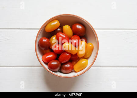 Varietà di organico cimelio di pomodori ciliegia nella ciotola sul bianco rustico tavolo in legno, overhead vista superiore direttamente dall'alto Foto Stock