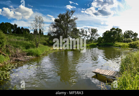 Piattaforma di legno per la pesca sul fiume in estate. La riflessione di alberi e cielo nell'acqua.0 Foto Stock