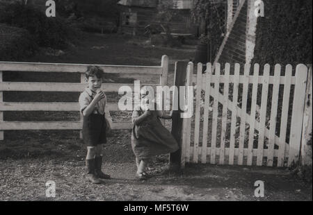 1936, storico, una infanzia rurale......ragazzo giovane e la sua sorella più giovane godere il loro cornet gelati in attesa al di fuori dei cancelli di ingresso alla loro azienda, Hampshire, Inghilterra, Regno Unito. Foto Stock