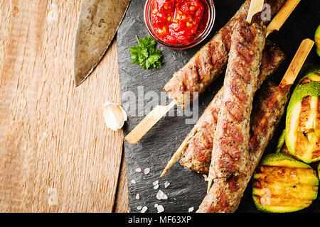 Tradizionali fatti in casa turca alla griglia Adana Urfa Kebab, carni macinate kebab, sulla piastra di ardesia con insalata di pomodoro e salsa sopra lo sfondo di legno Foto Stock