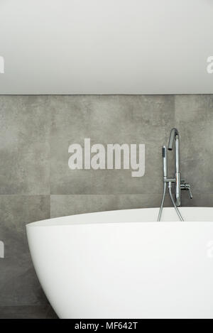 White vasca da bagno contro il muro grigio in semplice bagno interno sull attico Foto Stock