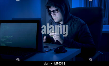 Giovane maschio hacker nel lavoro del cofano sul laptop per rubare i soldi dalla carta di credito Foto Stock