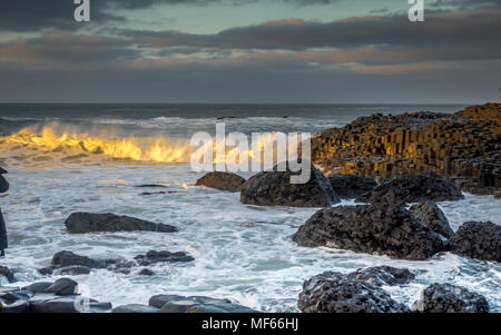 Le onde che si infrangono sulla roccia esagonale formazione al Giant Causeway appena prima del tramonto, Irlanda del Nord, Regno Unito Foto Stock