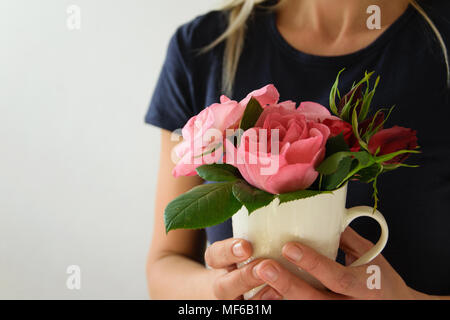 Giovane donna detiene una tazza con bellissime rose fresche Foto Stock