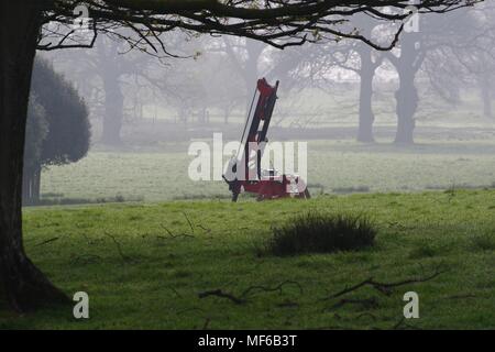 Macchine agricole, rosso trapano della coclea. Il Castello di Powderham Deer Park in una nebbiosa mattina di primavera. Exeter Devon, Regno Unito. Aprile, 2018. Foto Stock