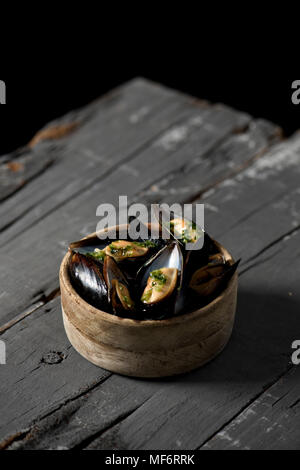 Primo piano di una ciotola di legno di bosso con moules mariniere, una ricetta francese di cozze, su una tavola in legno rustico Foto Stock