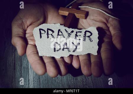 Primo piano delle mani di un giovane uomo caucasico con un crocifisso in legno e un pezzo di carta con il testo di preghiera nel giorno di loro Foto Stock