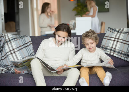 Piccolo figlio di fingere di leggere il giornale seduto sul divano con la fa Foto Stock