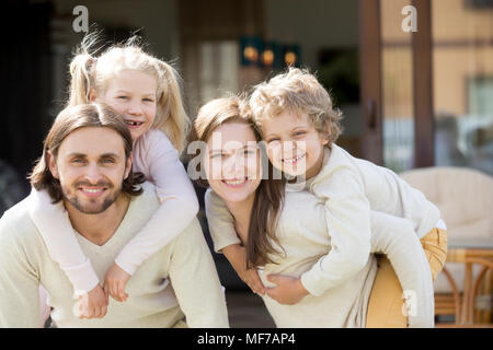 Genitori felici piggybacking bambini sul terrazzo della casa guardando è venuto Foto Stock