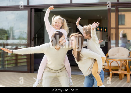 Sorridente genitori piggybacking giocando con i bambini a trascorrere del tempo Foto Stock