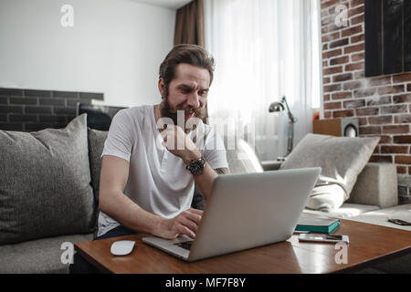 Uomo sorridente comodamente seduti sul divano di casa utilizzando laptop Foto Stock