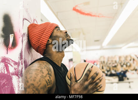 Uomo con tatuaggi e cappellino tenendo la pallacanestro Foto Stock