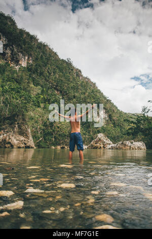 Cuba, Baracoa, giovane uomo in piedi nel fiume Yumuri, vista posteriore Foto Stock