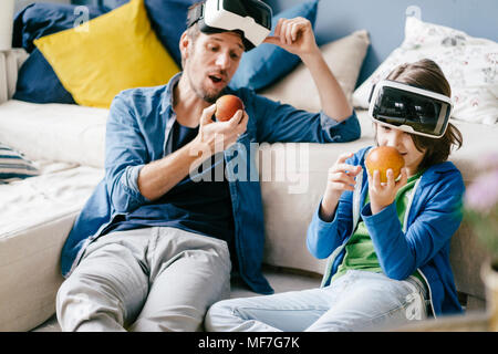 Padre e figlio indossando occhiali VR e mangiare le mele a casa Foto Stock