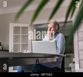 Malinconici uomo maturo seduta a tavola con il computer portatile nel suo salotto Foto Stock