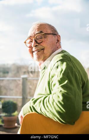 Ritratto di sorridere senior uomo seduto su una sedia in corrispondenza della finestra Foto Stock