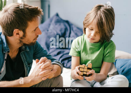 Padre guardando il figlio giocare con un cubo a casa Foto Stock