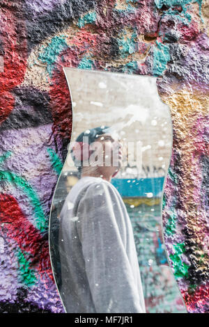 Immagine speculare del giovane con le cuffie guardando graffiti Foto Stock