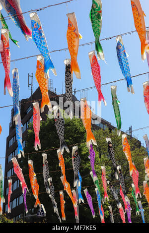 Molte colorate di carpe di carta o a forma di pesce lanterne,chiamato koinobori, appendere su funi infilate overhead diagonalmente contro un cielo blu. La luce del sole li colpisce. Foto Stock