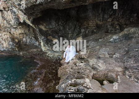 Giovane sposi sposa e lo sposo ride e sorrisi a ciascun altro, felice e gioioso momento. L uomo e la donna nel matrimonio abiti sedersi sulla roccia dello sfondo. Foto Stock