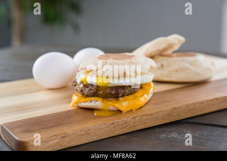 Salsicce, uova e formaggio colazione panino con muffin inglese sul tagliere con forcella in esecuzione Foto Stock