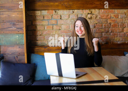 Lucky donna godendo di vincere le scommesse online dal computer portatile presso il cafe. Foto Stock