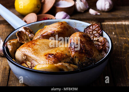 Pollo arrosto con aglio, timo e limone nella padella di cottura rustico sfondo di legno Foto Stock