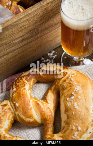 In casa Pretzel con sale marino e bicchiere di birra su tavola in legno rustico Foto Stock