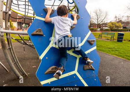 Un giovane ragazzo si inerpica su una parete da arrampicata in un parco giochi per bambini al centro del villaggio di Perton vicino a Wolverhampton. Foto Stock