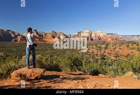 Giovane atletico maschile che fotografa paesaggi desertici Ponte del Diavolo percorso escursionistico Sedona Arizona Sunny Winter Day Scenic Red Rock Formations Blue Skyline Foto Stock