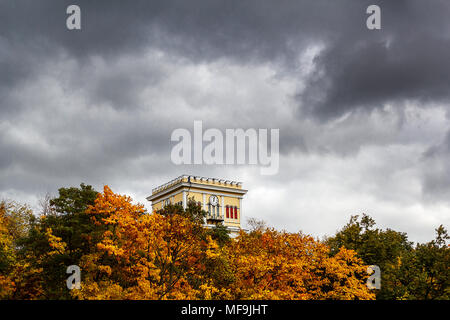 Un edificio alto con un orologio contro un avvicinamento tempesta nel cielo. Un antico edificio tra il fogliame e si avvicina il temporale Foto Stock