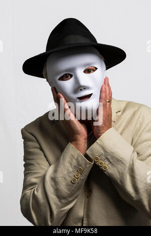 L'uomo bianco che indossa la maschera per il viso, black hat, e camicia di lino contro uno sfondo bianco Foto Stock