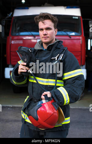 Bel giovane vigile del fuoco tenendo tubo antincendio in uniforme Foto Stock