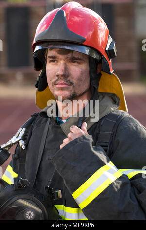 Bel giovane vigile del fuoco tenendo tubo antincendio in uniforme Foto Stock