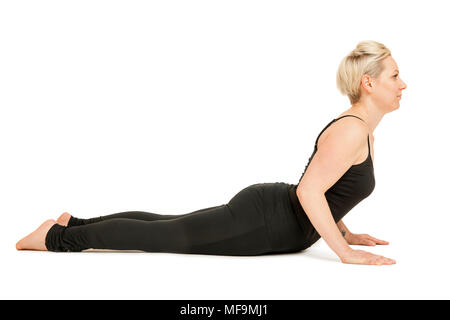 Seitliche Ganzkörper-Ansicht einer blondn Frau mittleren altera im schwarzen Sportdress vor weißen Hintergrund die Yoga-Übung die Kobra (Bhujangasana Foto Stock