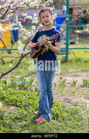 Una bambina gioca ukulele nel giardino. Foto Stock