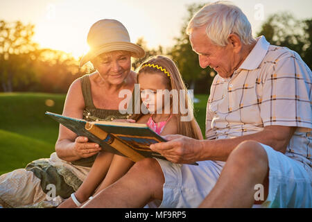 Ragazza con i nonni, album fotografico. La gente guarda foto all'aperto. Molti anni fa. Foto Stock