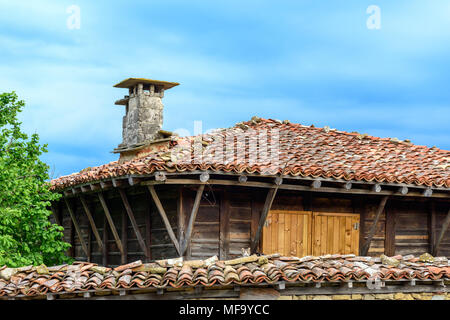 Zheravna, Bulgaria - unica autentica casa rustico in pietra e legno con chiusura persiane in legno e tetto di tegole contro il cielo blu Foto Stock