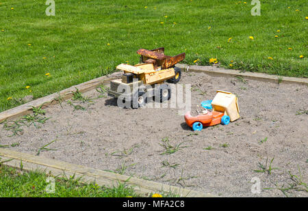 Vecchi giocattoli usurato in una sandbox circondato da erba verde all alcuni denti di leoni. Foto Stock