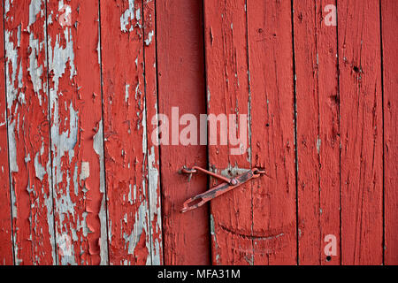 La vita di un antico granaio rosso porta con peeling vernice vecchia e letti in ferro battuto con gancio Foto Stock