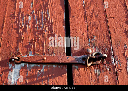 La vita di un antico granaio rosso porta con peeling vernice vecchia e letti in ferro battuto con gancio Foto Stock