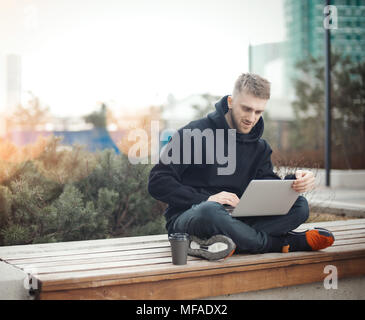 Sorridente giovane azienda laptop sulle ginocchia. Black Coffee Cup è accanto a lui. Foto Stock