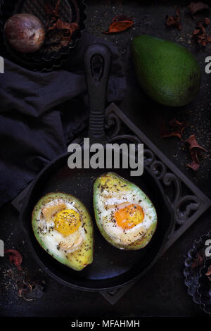 Cotta di avocado con uovo e brie in una ghisa pan su sfondo scuro Foto Stock