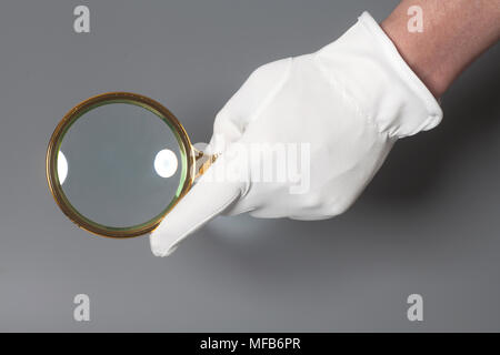 Gli uomini la mano nel guanto bianco azienda golden lente di ingrandimento Foto Stock