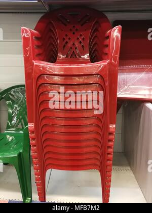 Impilati in righe di rosso le sedie in plastica sulla vetrina. Foto Stock