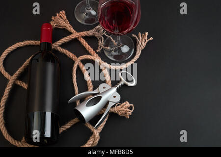 Rosso bottiglia di vino, due bicchieri e cavatappi su sfondo nero. Vista da sopra con lo spazio di copia Foto Stock