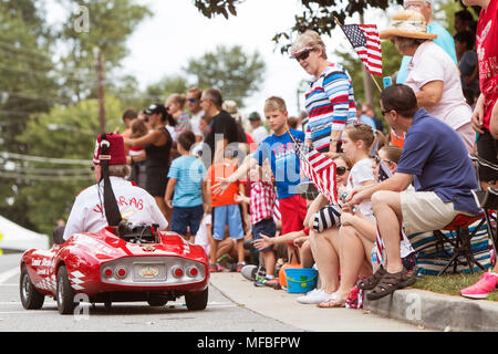 Famiglie sedersi sul cordolo con bandierine americane e di interagire con le persone su il percorso della parata del vecchio soldato sfilata il 1 agosto 2015 in Alpharetta, GA. Foto Stock